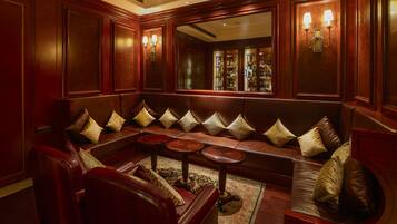 A luxurious lounge area with a leather sofa, round tables, and a bar with a mirrored wall.