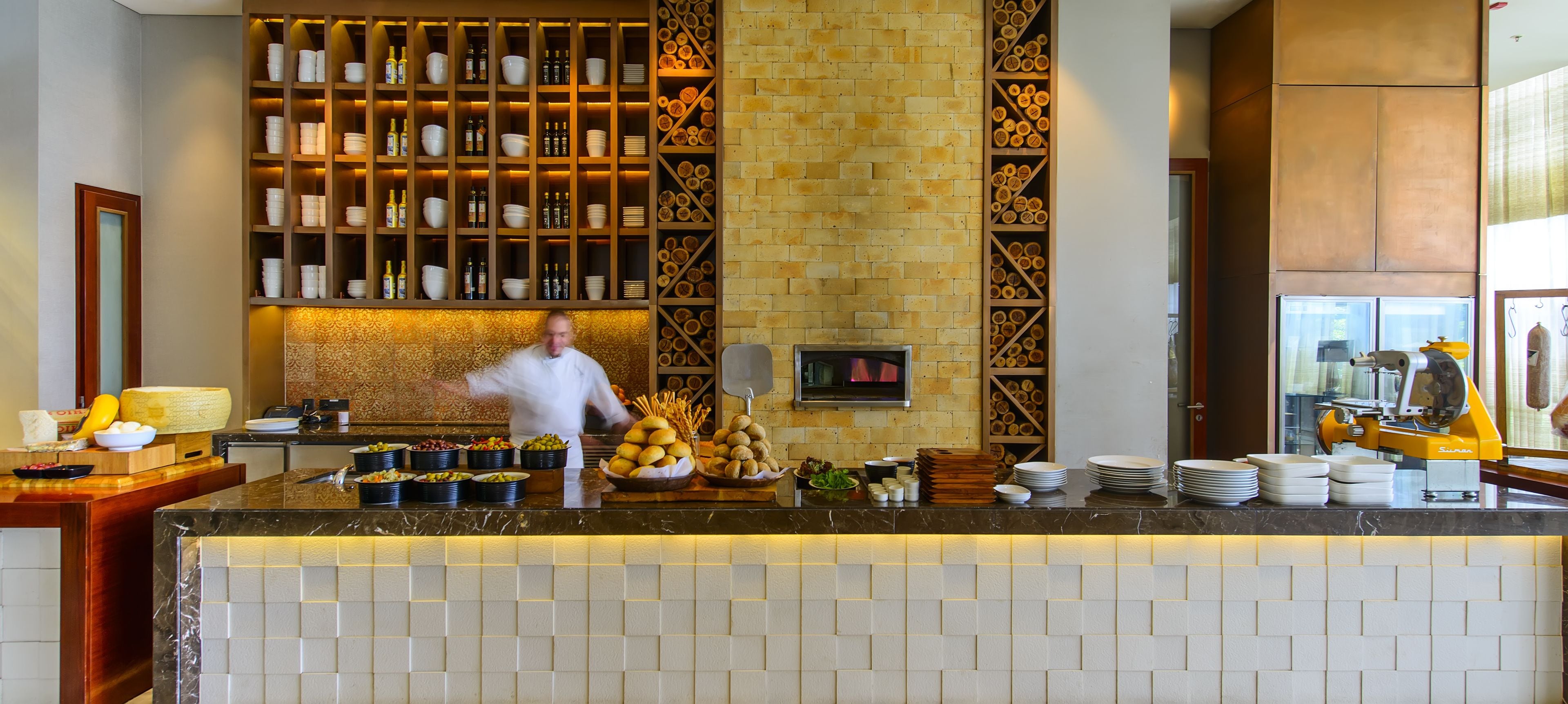 A chef preparing food in a well-equipped kitchen with a marble countertop, various food items, and a brick wall with shelves.