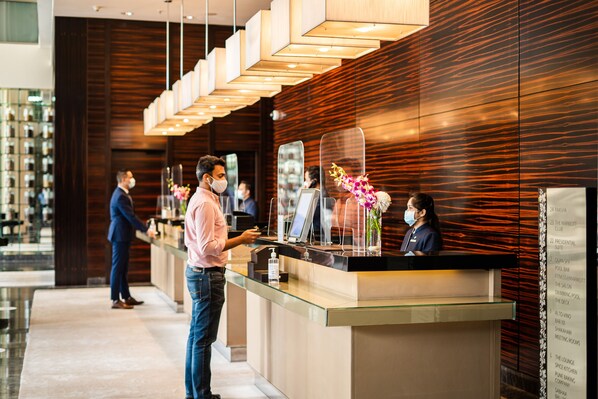 A hotel reception area with a modern design, featuring a reception desk, a digital display, and a glass partition.