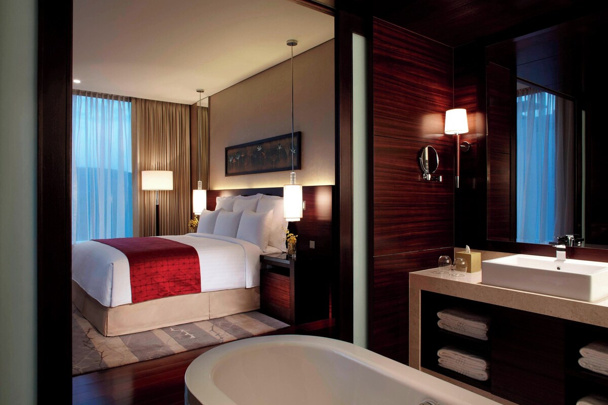 A hotel room with a large bed, a bathroom with a sink and mirror, and a view of the city.