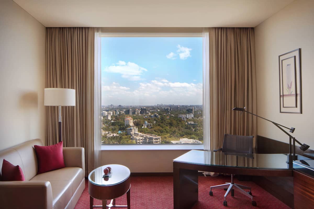 Una habitación de hotel con un ventanal grande, un sofá, un escritorio y una lámpara.