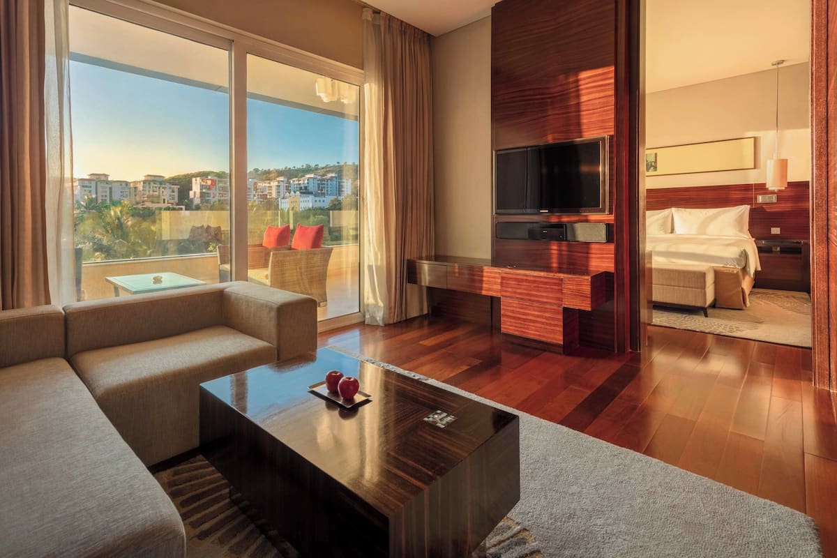 Una habitación de hotel moderna con un balcón grande, un sofá, una mesa de centro, un televisor y una cama.