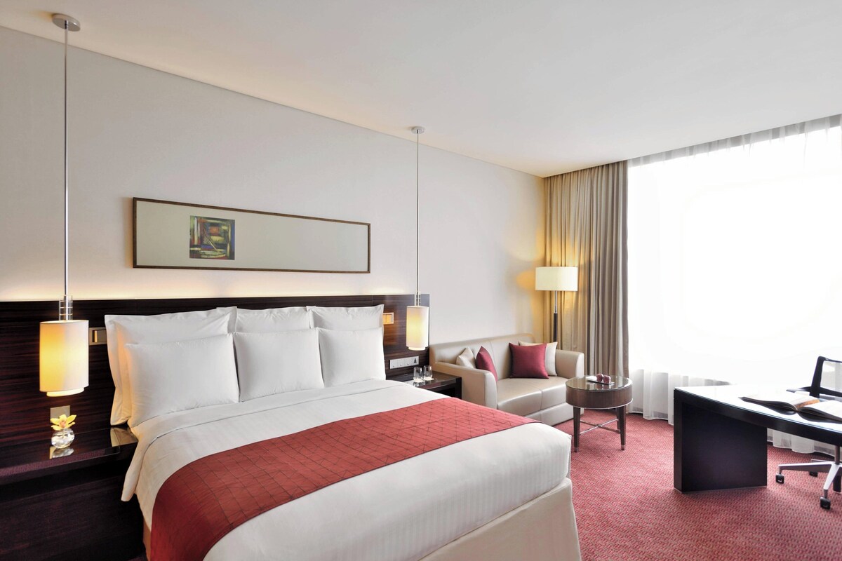 A hotel room with a large bed, a desk, a chair, a sofa, and a window with curtains.
