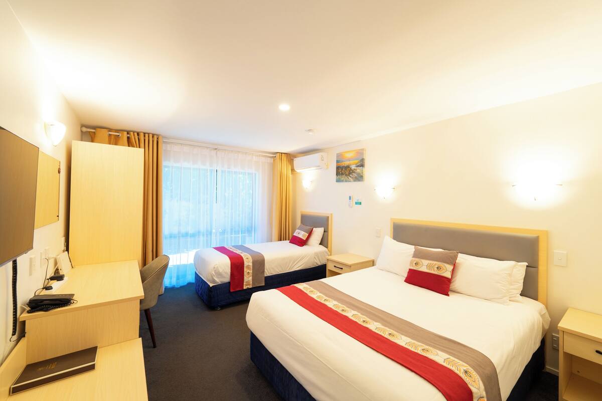A hotel room with two beds, a desk, a chair, and a TV.