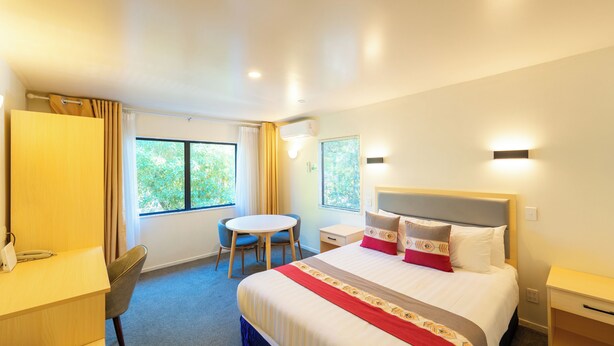 A hotel room with a bed, a desk, a chair, a small table, and a window. - Auckland Newmarket Motel (Auckland)