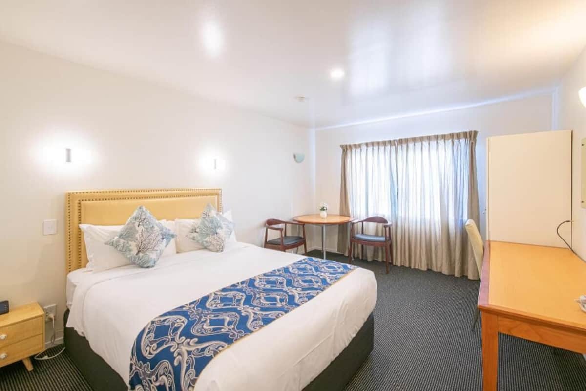 A hotel room with a bed, a desk, a chair, a small table, and a window with curtains.