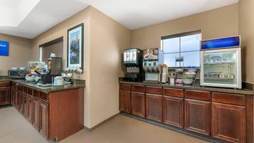 Una cocina de hotel con una estación de café, un refrigerador y un microondas.