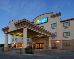 A Comfort Inn hotel with a covered entrance, multiple windows, and a clear sky.