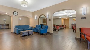A hotel lobby with a blue sofa set, a clock, and a dining area in the background. - Comfort Inn I-20 Midland Stanton (Stanton)