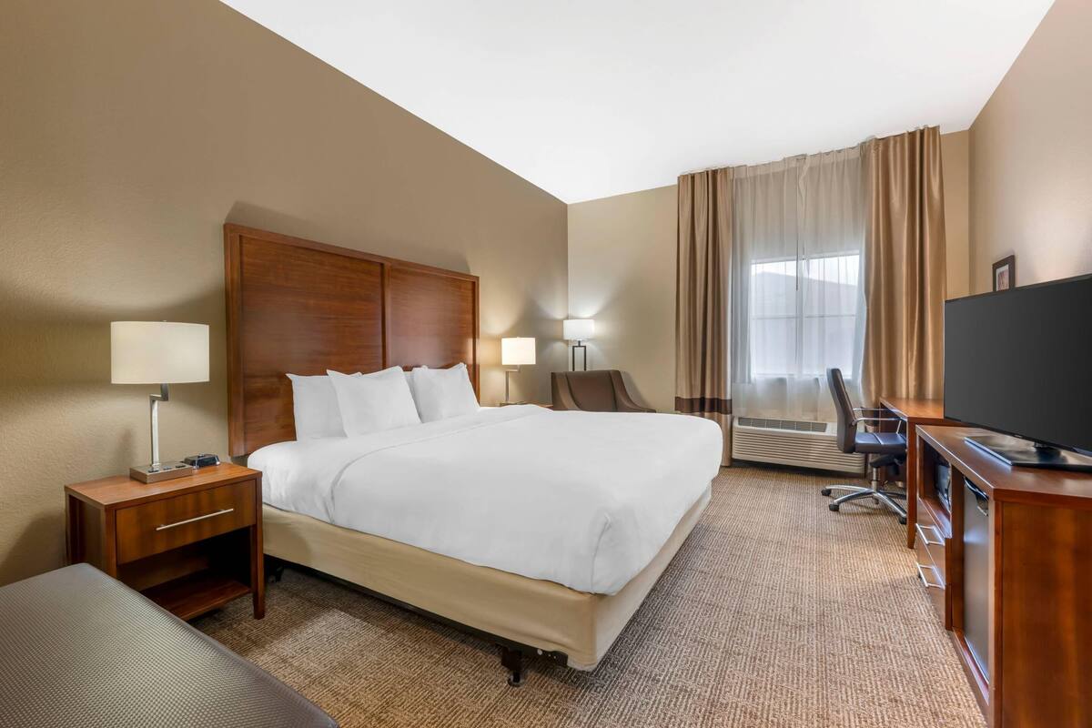 A hotel room with a large bed, a desk with a computer, a TV, and a chair.