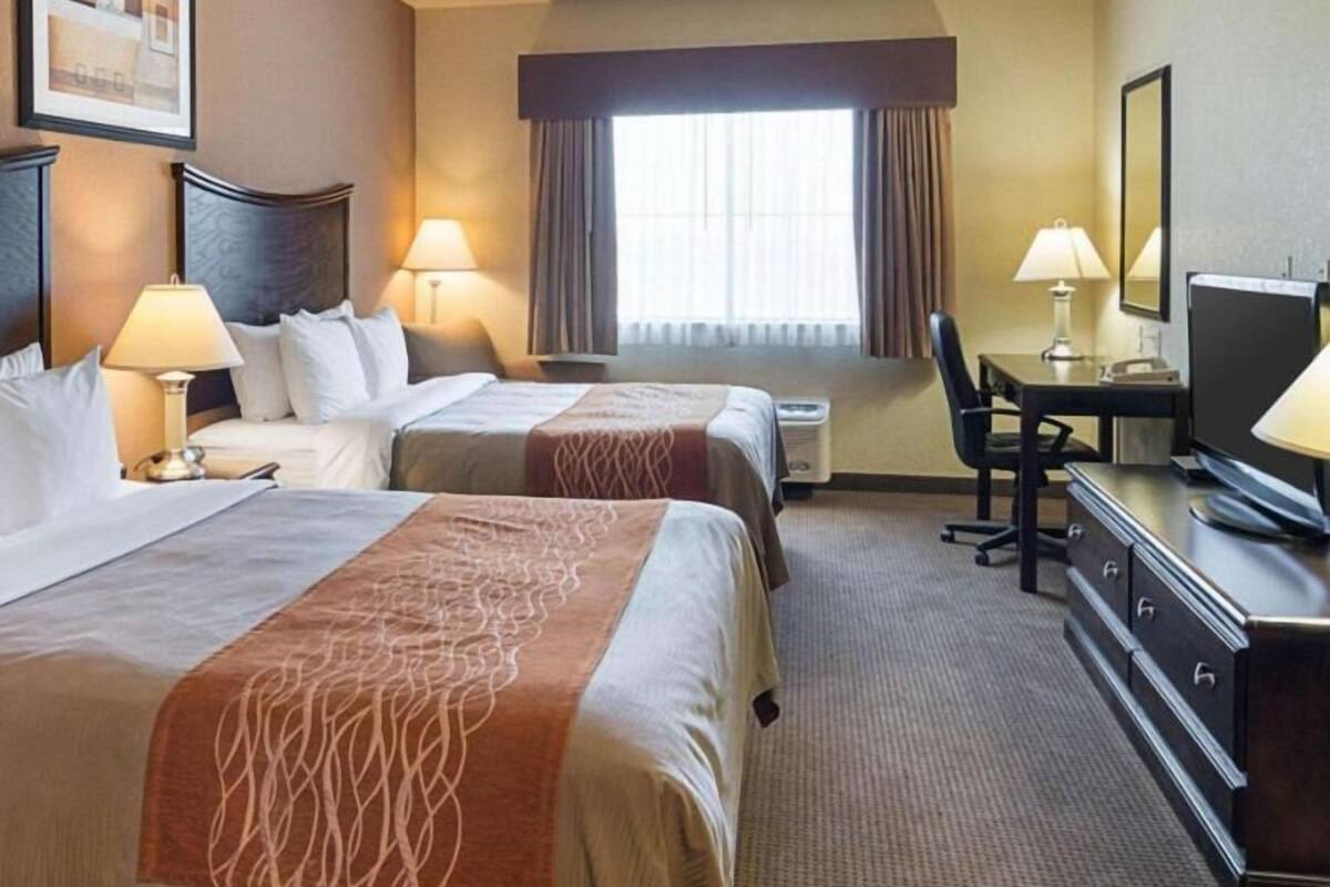 A hotel room with two beds, a desk, a chair, a television, and a window with curtains.