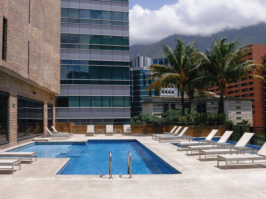 A swimming pool with lounge chairs, a brick building, and a modern glass building in the background.
