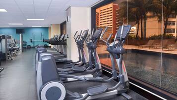 Un gimnasio con cintas de correr, máquinas de pesas y un amplio ventanal con vistas a una zona de piscina.