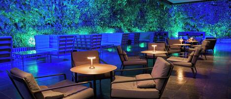 A modern lounge area with seating and tables, a green wall with plants, and ambient lighting.