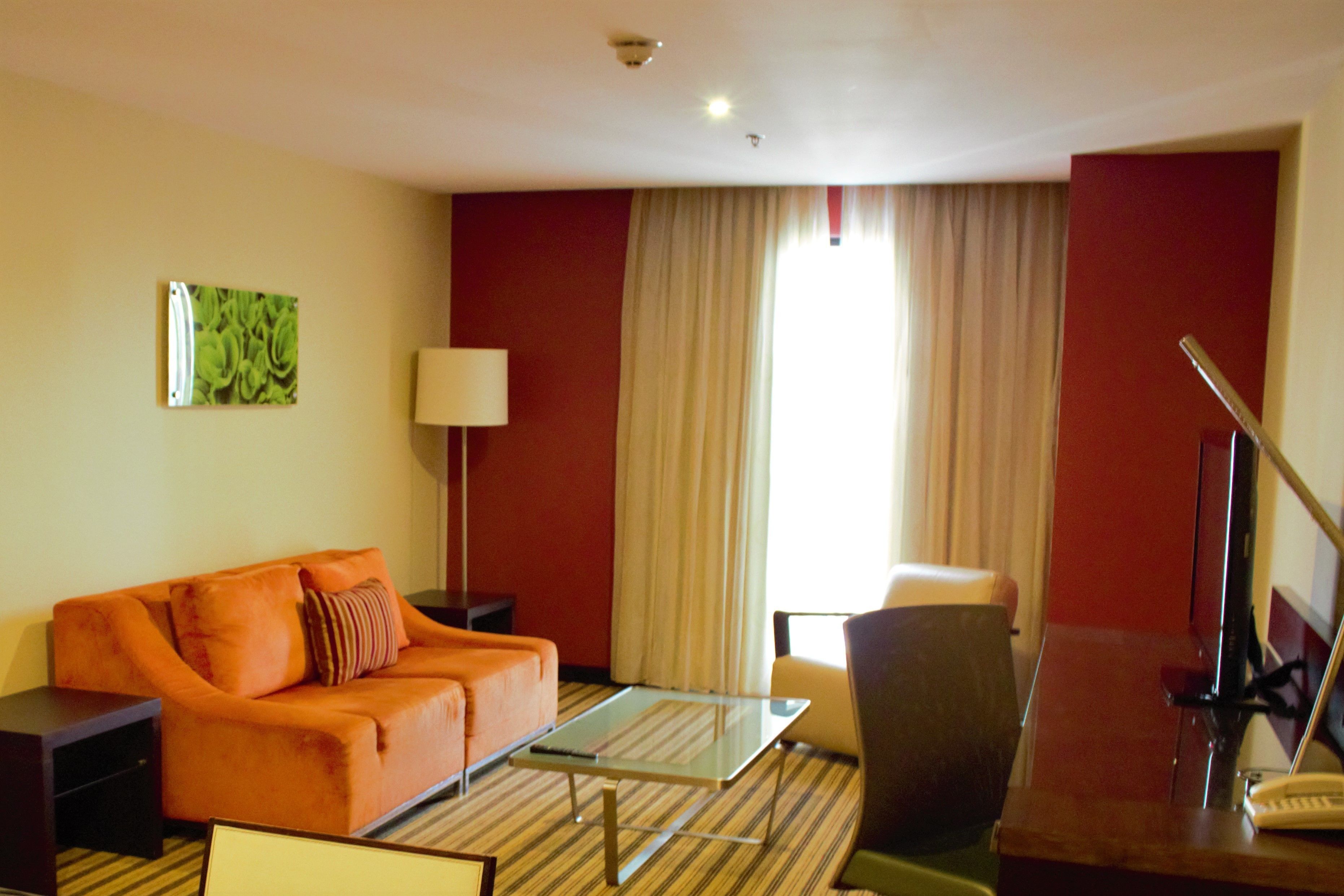 Habitación de hotel con sofá, mesa de centro, escritorio con lámpara y una silla.