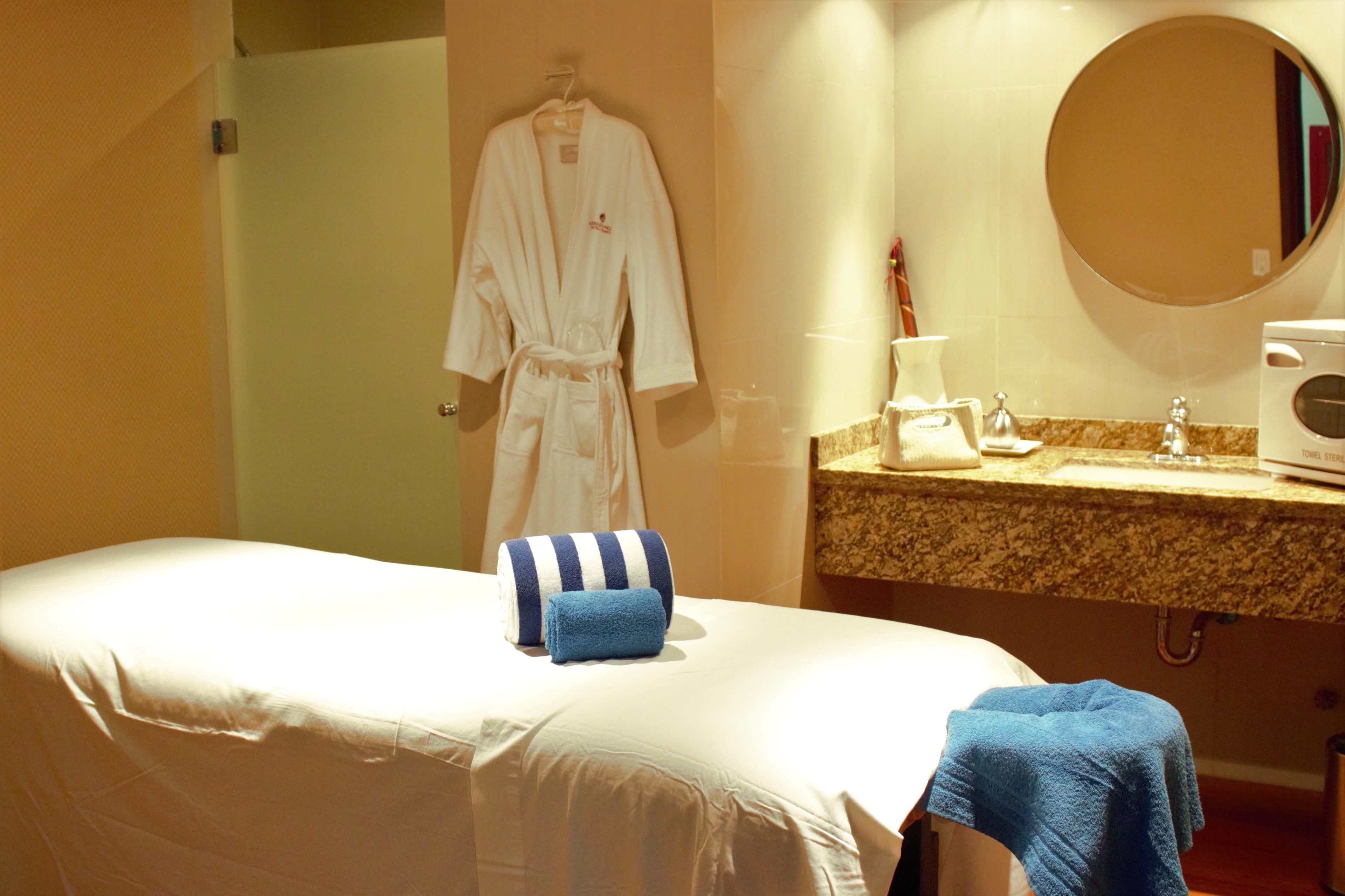 A hotel room with a massage table, a robe hanging on the wall, a sink, and a mirror.
