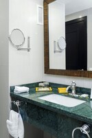 Un baño con lavamanos blanco, encimera de mármol verde y un espejo grande con marco de madera.