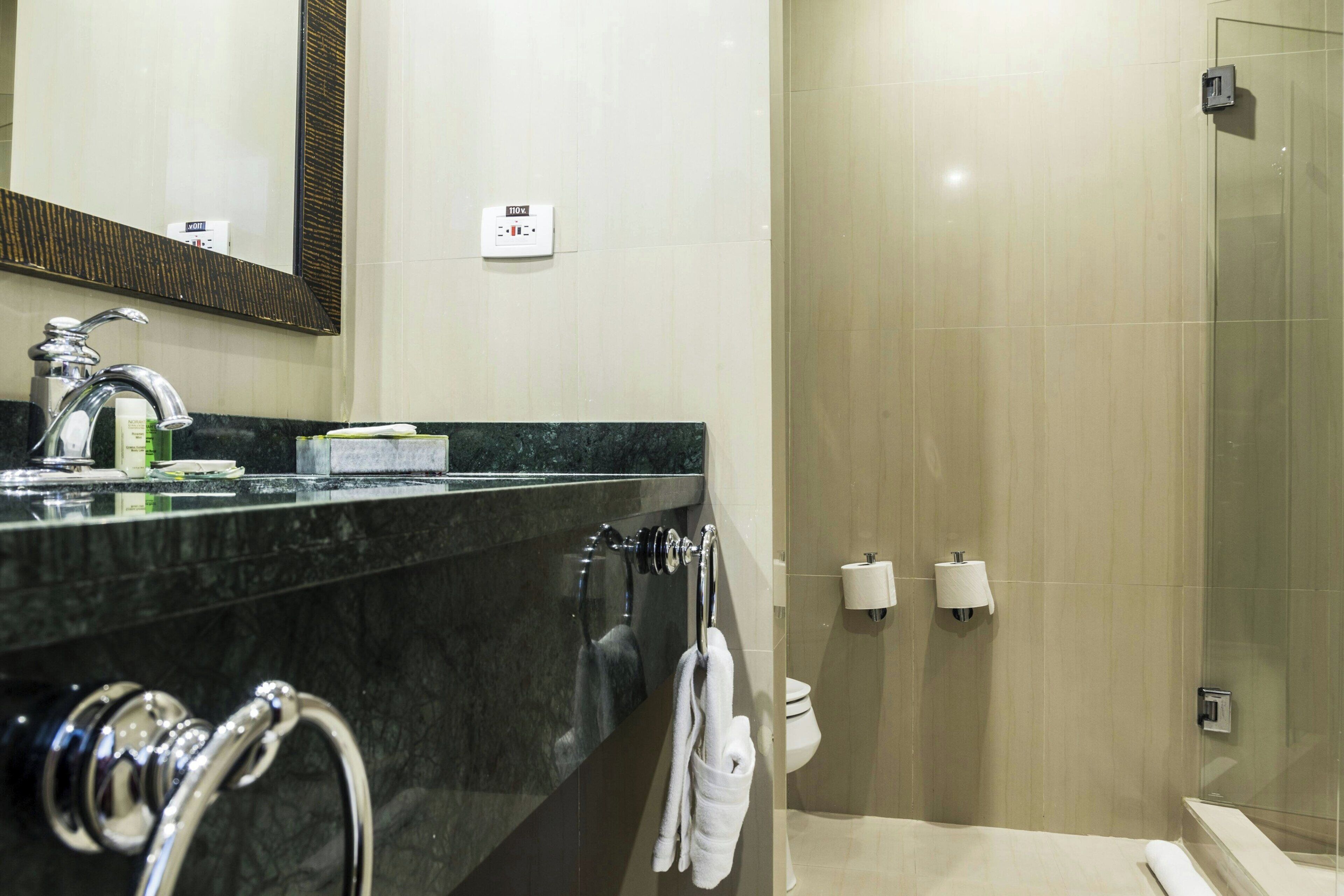 Une salle de bain moderne avec un lavabo en marbre, une cabine de douche en verre et un porte-serviettes.