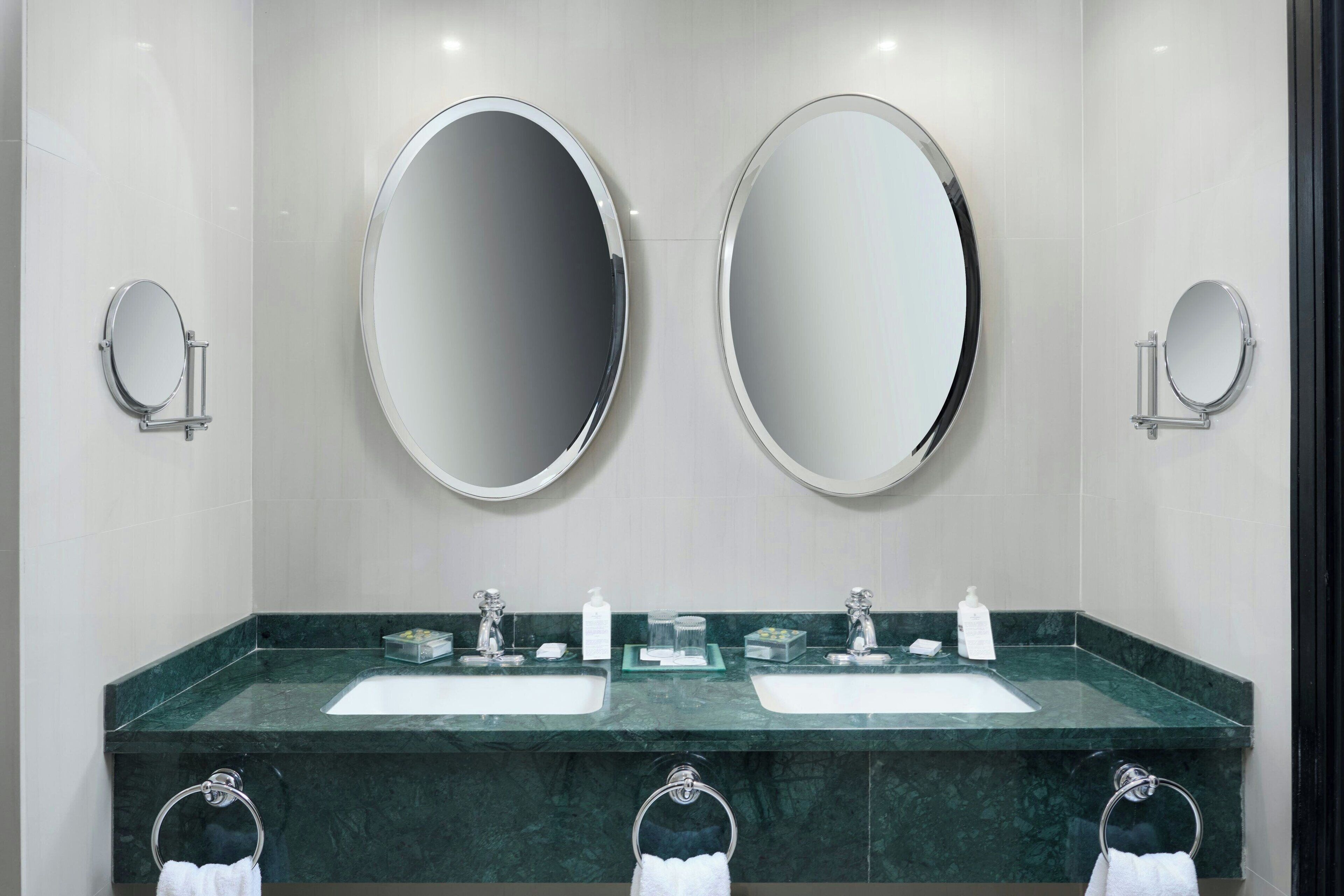 A bathroom with two sinks, two mirrors, and three towel rings.