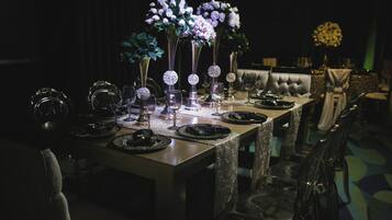 Una larga mesa de comedor adornada con varios jarrones de flores, copas de cristal y platos negros.