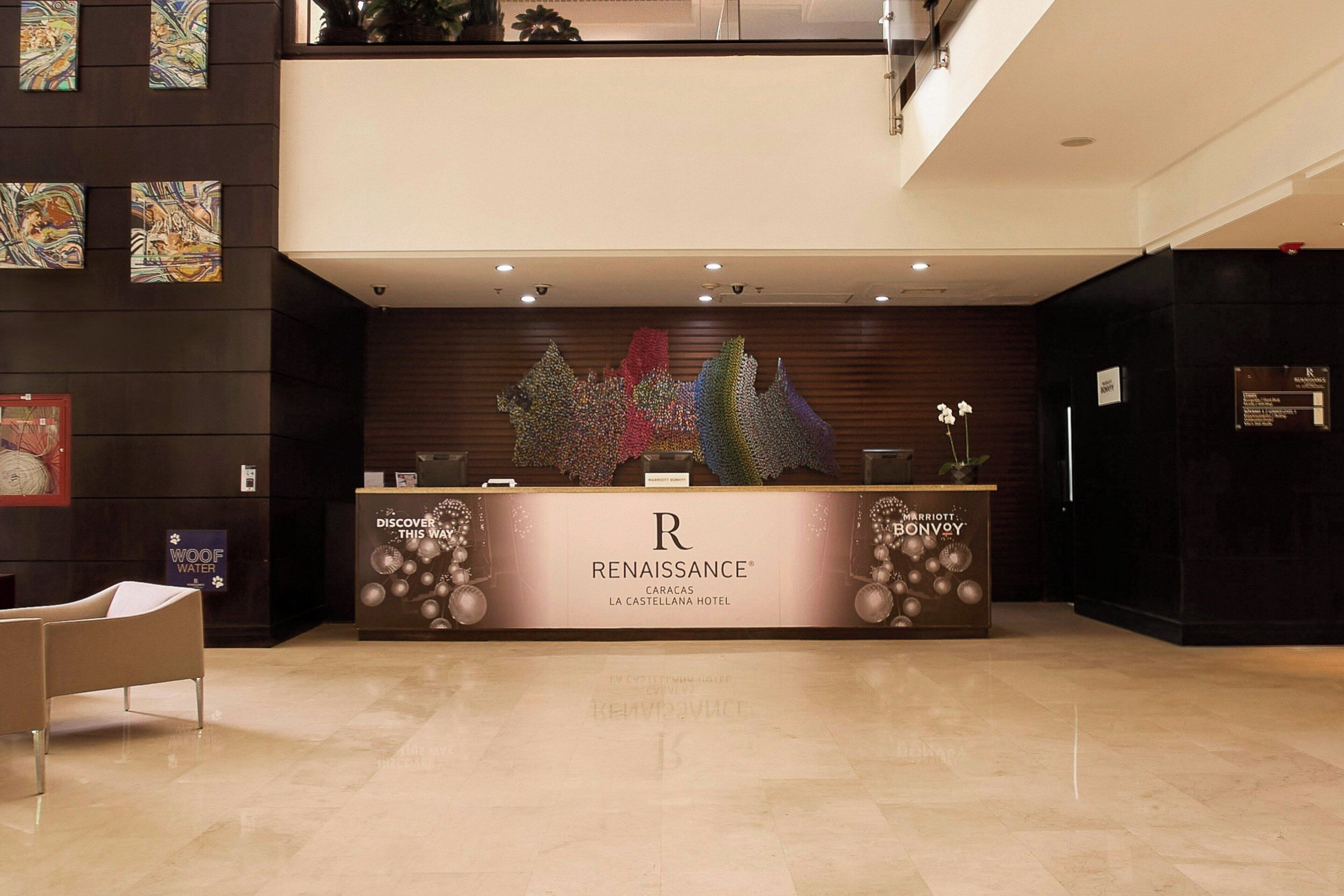 A reception desk at the Renaissance Caracas La Castellana Hotel with a modern design, a large abstract art piece above it, and a sign indicating the hotel's name.