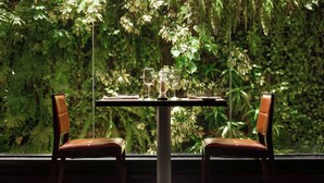 A dining table with two chairs, set for two, in front of a lush green wall. - Renaissance Caracas La Castellana Hotel (Caracas)