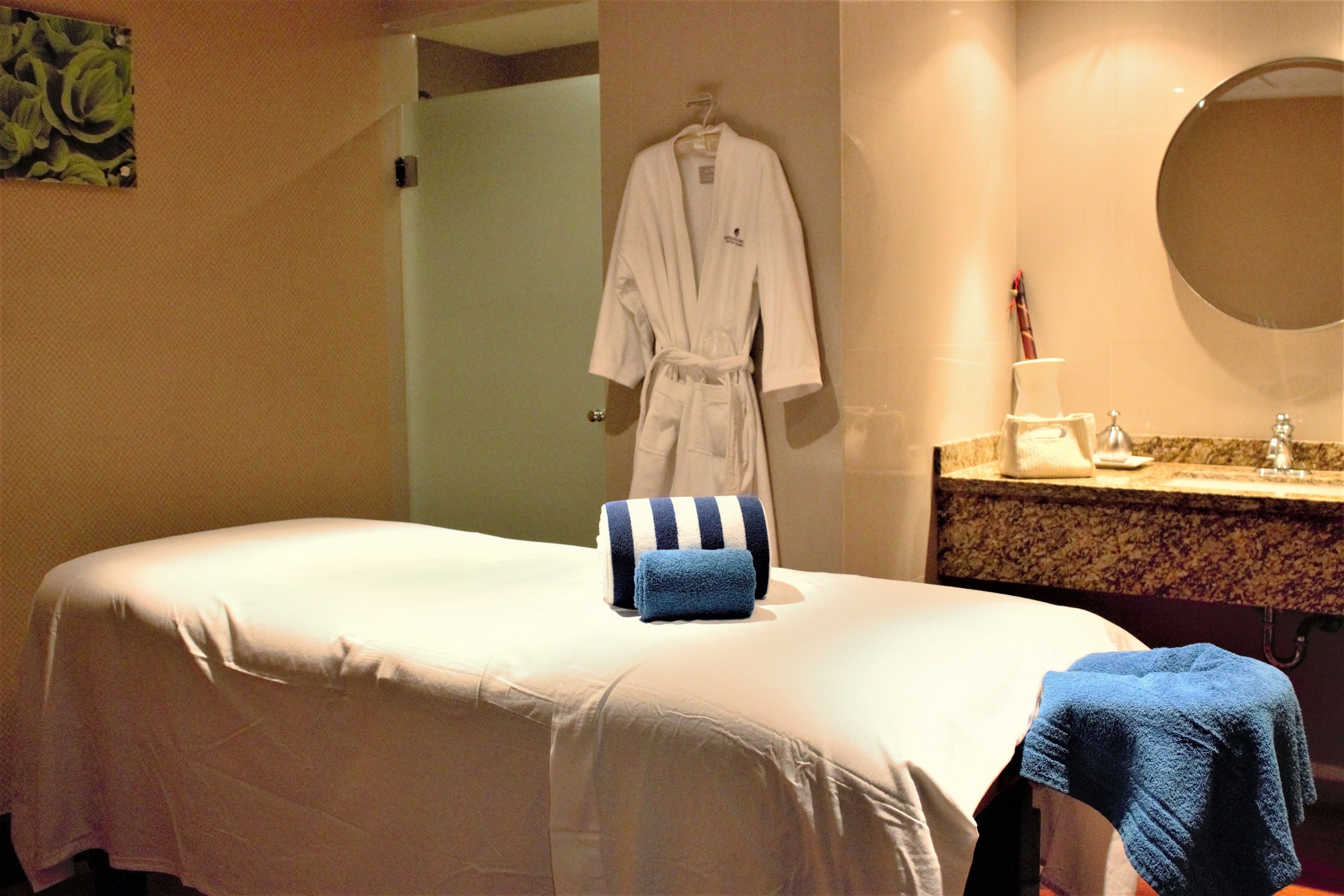 A hotel room with a bed, a robe hanging on the wall, a sink, and a mirror.