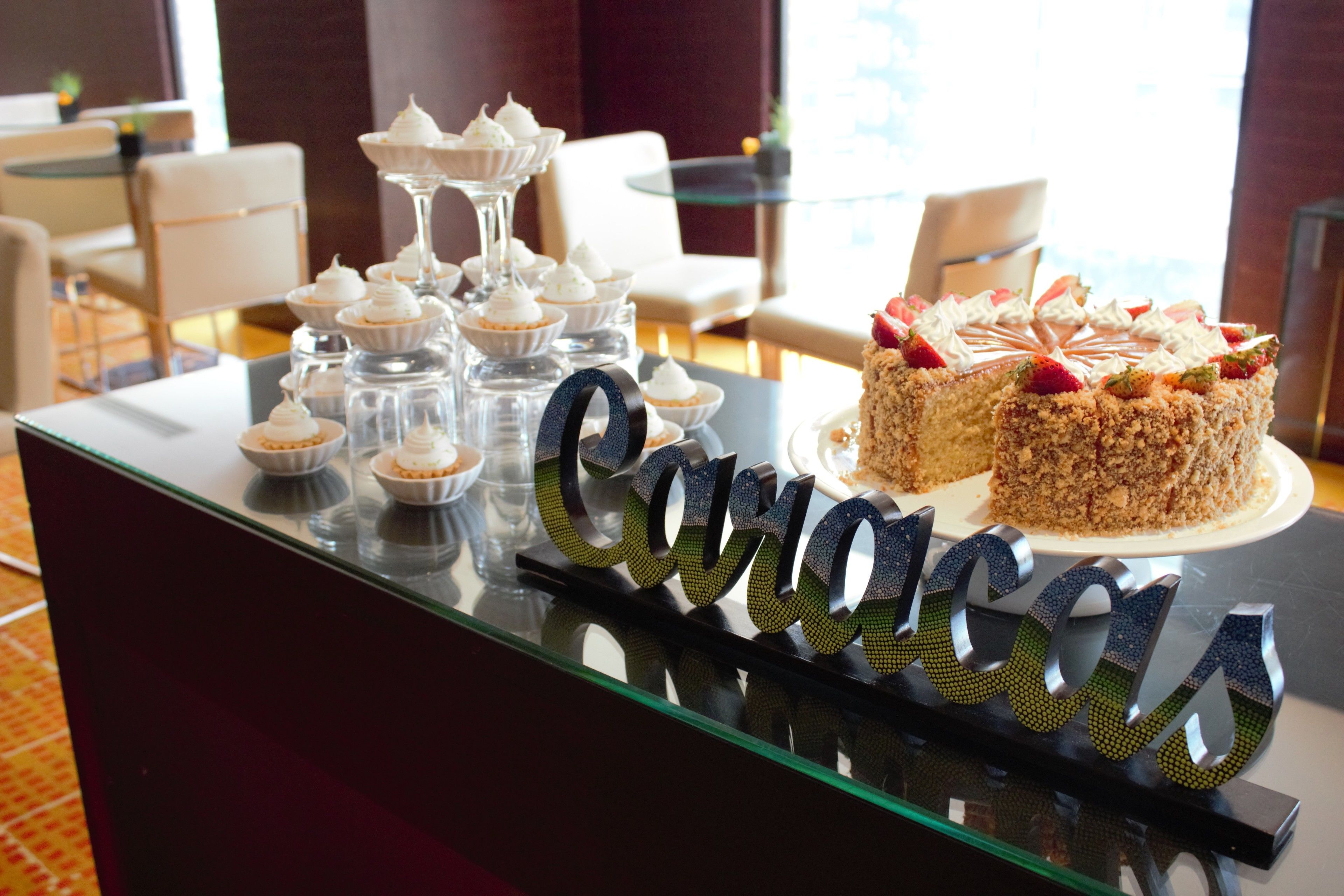 Una presentación de postres con diversos pasteles y dulces sobre un mostrador de vidrio en el vestíbulo de un hotel.