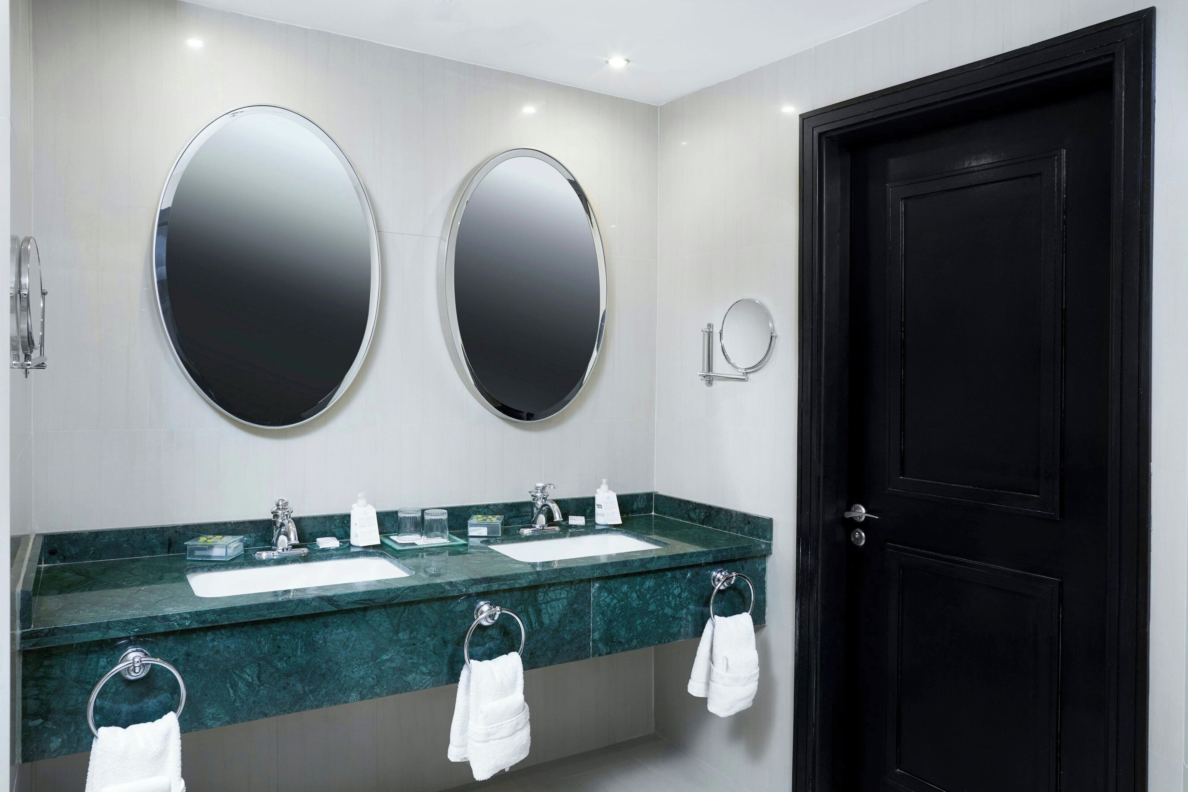 Une salle de bain avec deux lavabos, un grand miroir et une porte noire.