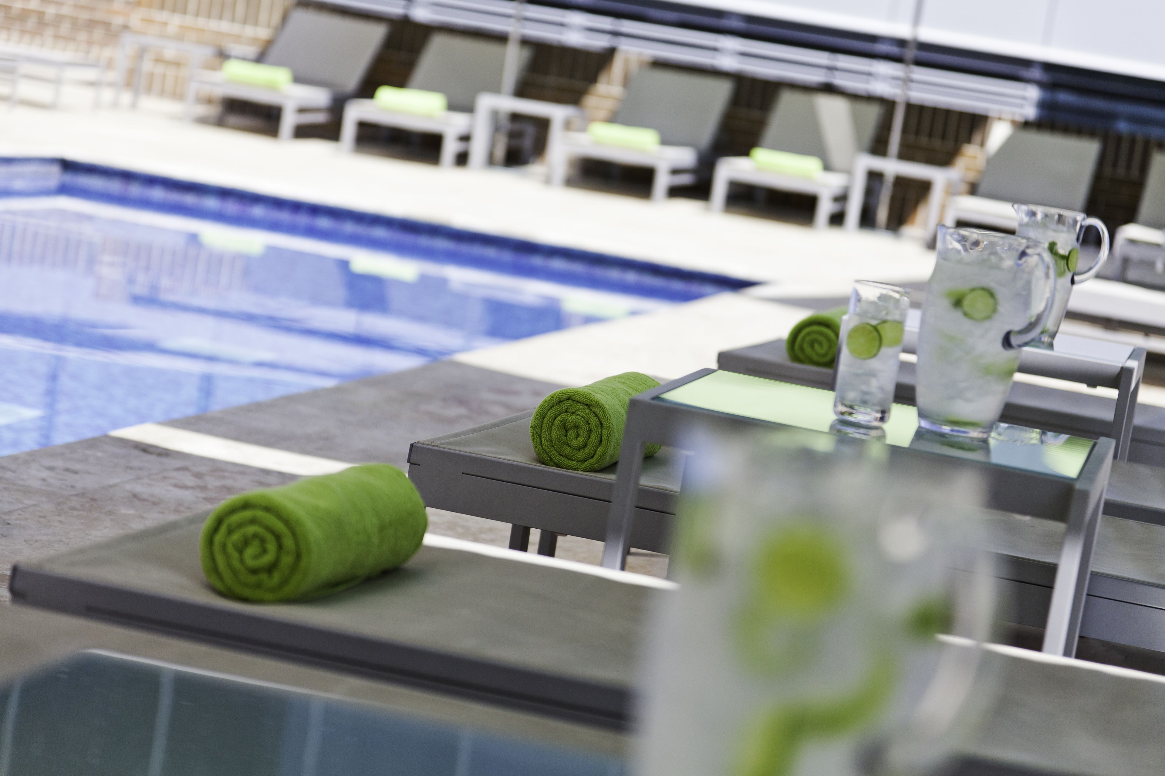 A poolside area with lounge chairs and a table with a pitcher of water and a glass.