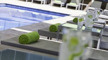 A poolside area with lounge chairs and a table with a pitcher of water and a glass.