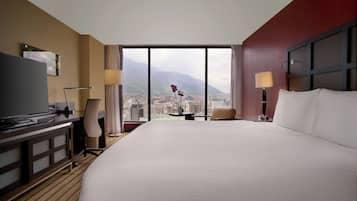 Une chambre d’hôtel avec un grand lit, un bureau, une chaise, une télévision et une vue sur la ville et les montagnes.