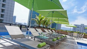 A rooftop pool area with lounge chairs and umbrellas, a pool, and a cityscape in the background. - Renaissance Caracas La Castellana Hotel (Caracas)