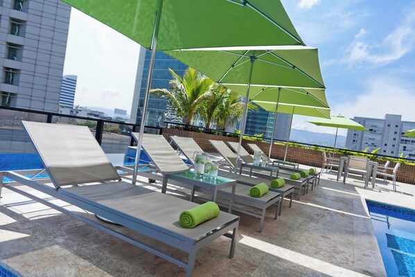 A rooftop pool area with lounge chairs and umbrellas, a pool, and a cityscape in the background. - Renaissance Caracas La Castellana Hotel (Caracas)