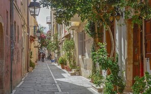 A narrow cobblestone street lined with buildings, some with balconies and potted plants. - Creta Aquamarine hotel (Rethymno)