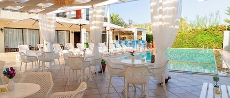 A poolside area with white wicker furniture, a bar, and a view of a pool.