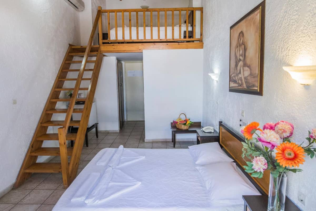Een slaapkamer met een stapelbed, een houten ladder, een nachtkastje met lamp en een vaas met bloemen.