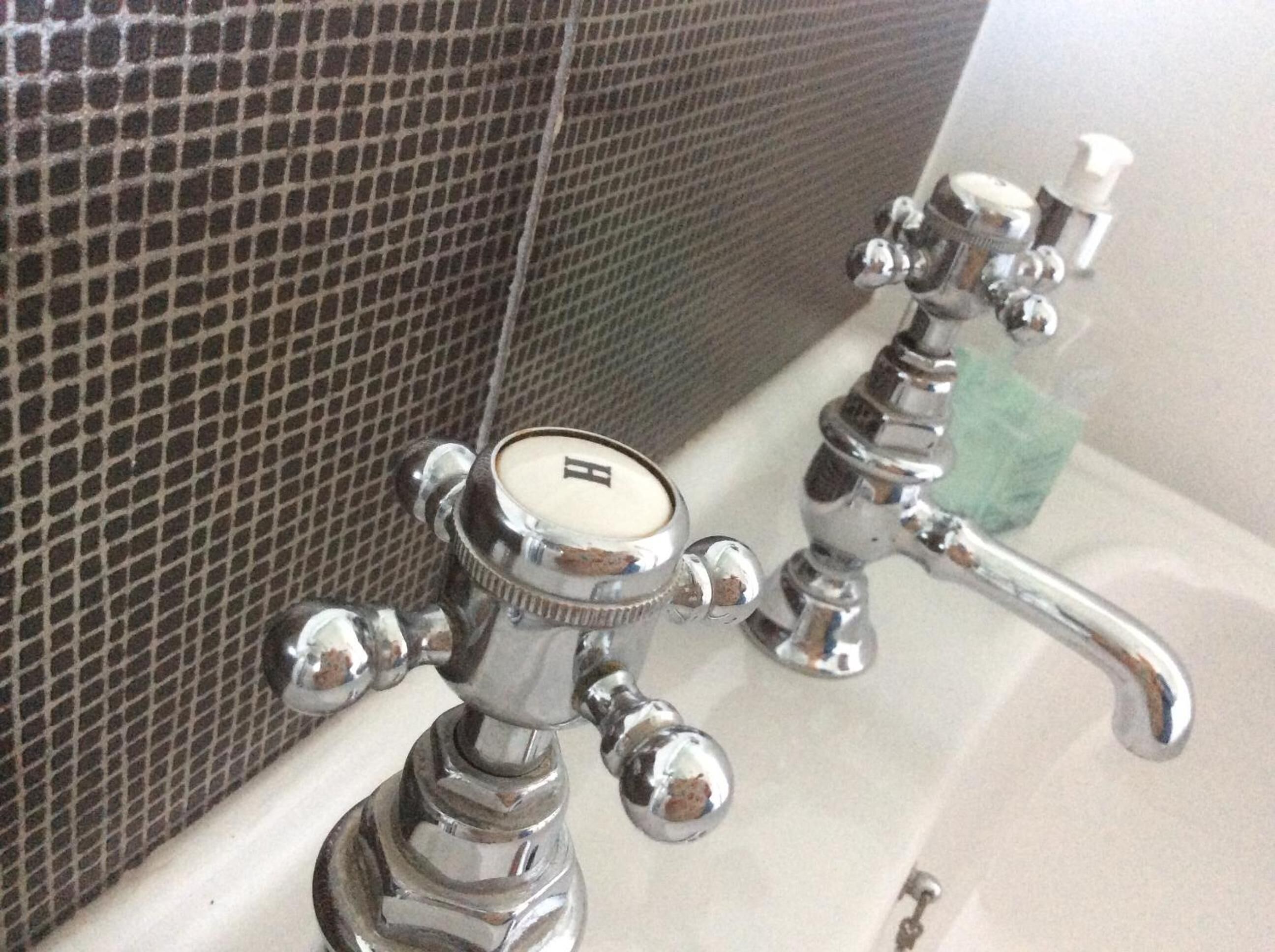 A bathroom with a tiled wall and two chrome faucets.