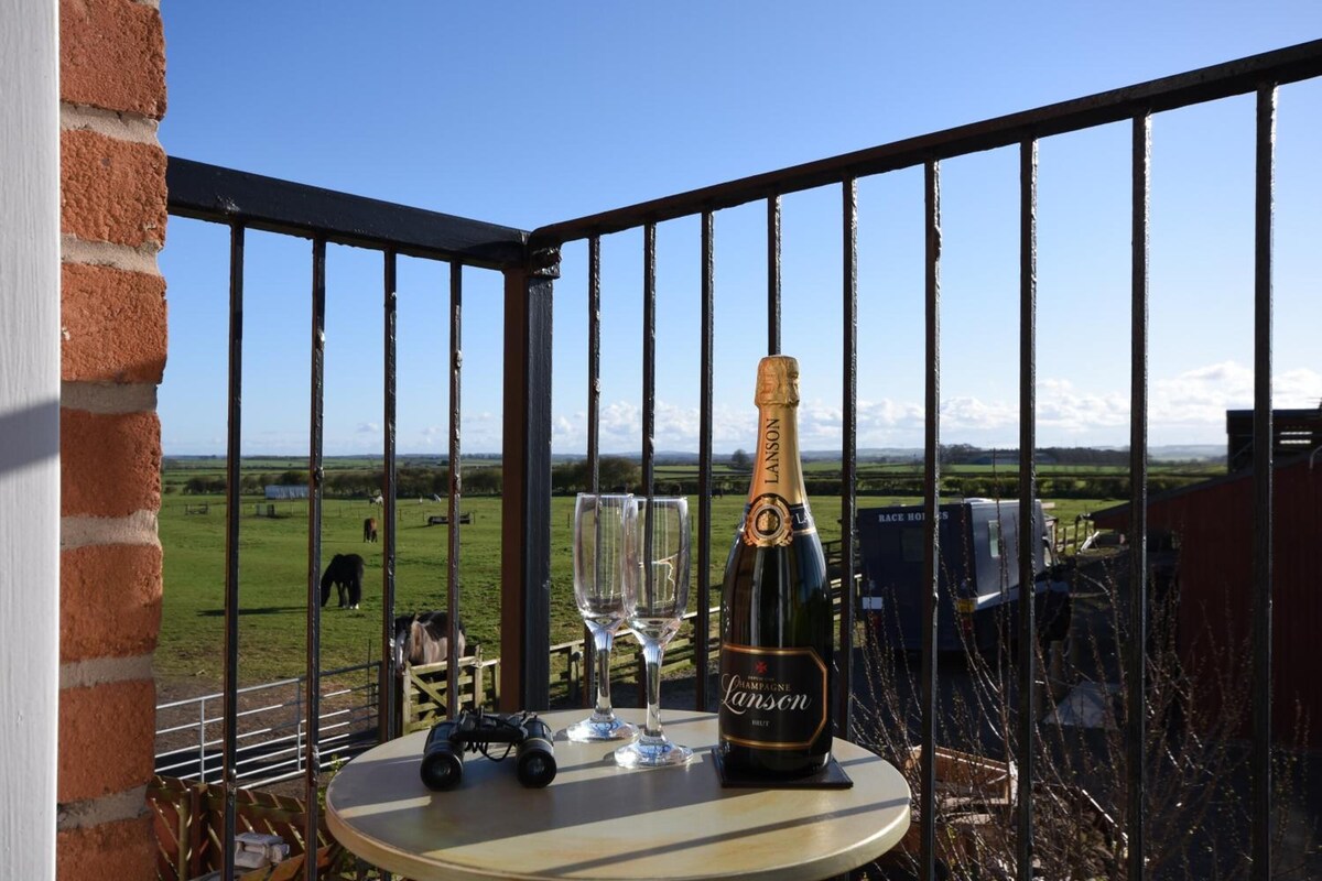 A balcony with a bottle of champagne, two glasses, and a toy car on a table.