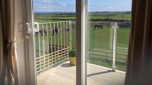 A balcony with a view of a grassy field and a stone wall.
