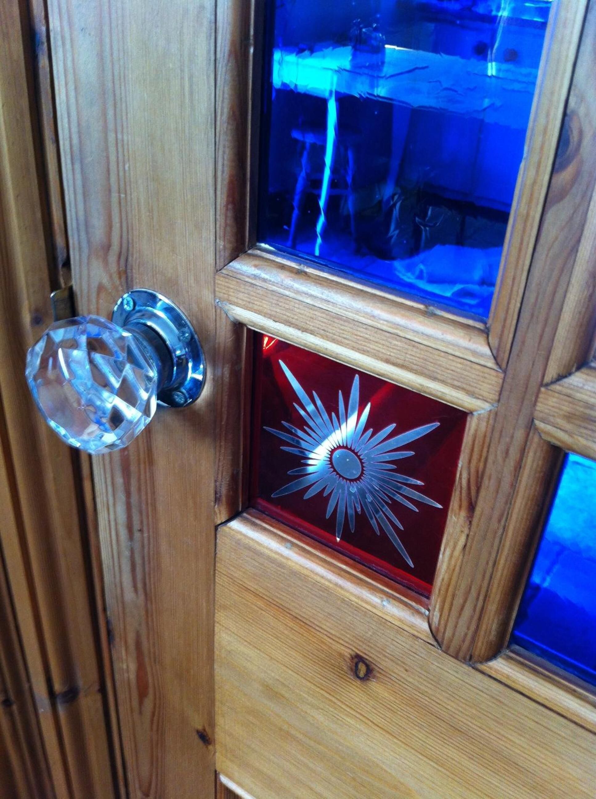 A wooden door with a clear crystal handle and a decorative glass panel with a sunburst design.