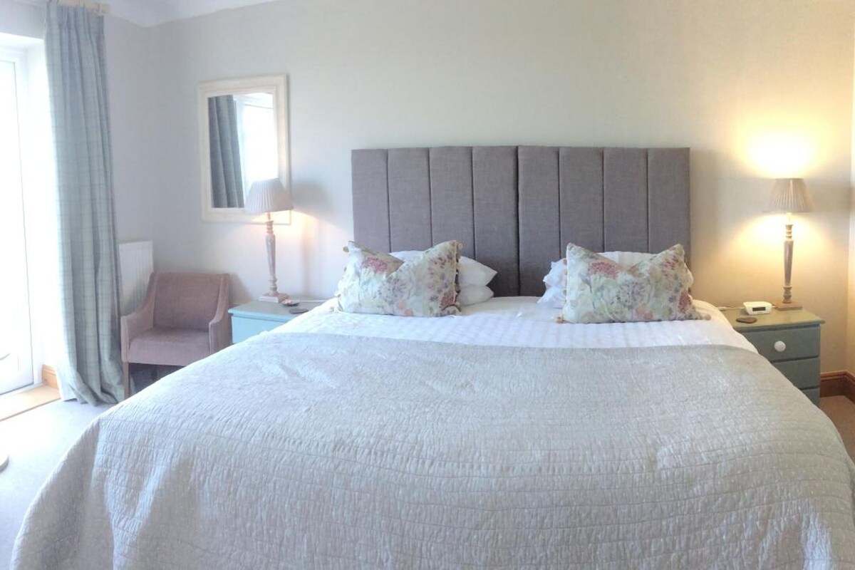 A neatly arranged bedroom with a large bed, two bedside tables, a chair, and a window with curtains.