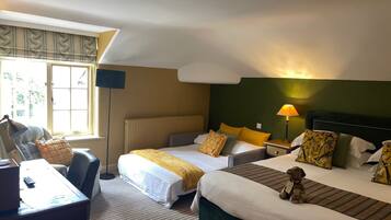 A hotel room with two beds, a desk, a chair, a lamp, and a window with blinds.