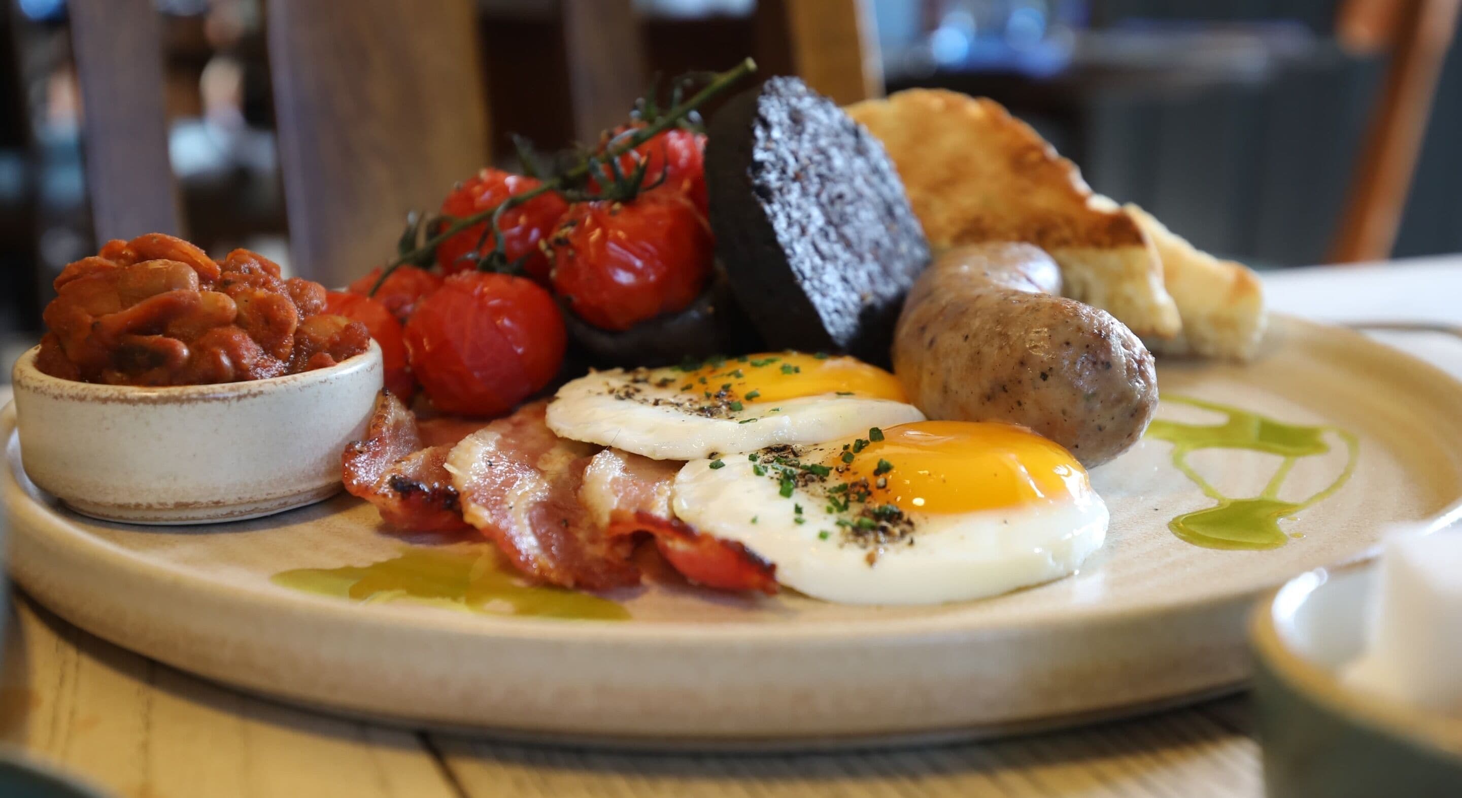 En frukosttallrik med ägg, bacon, korv, tomater och rostat bröd.