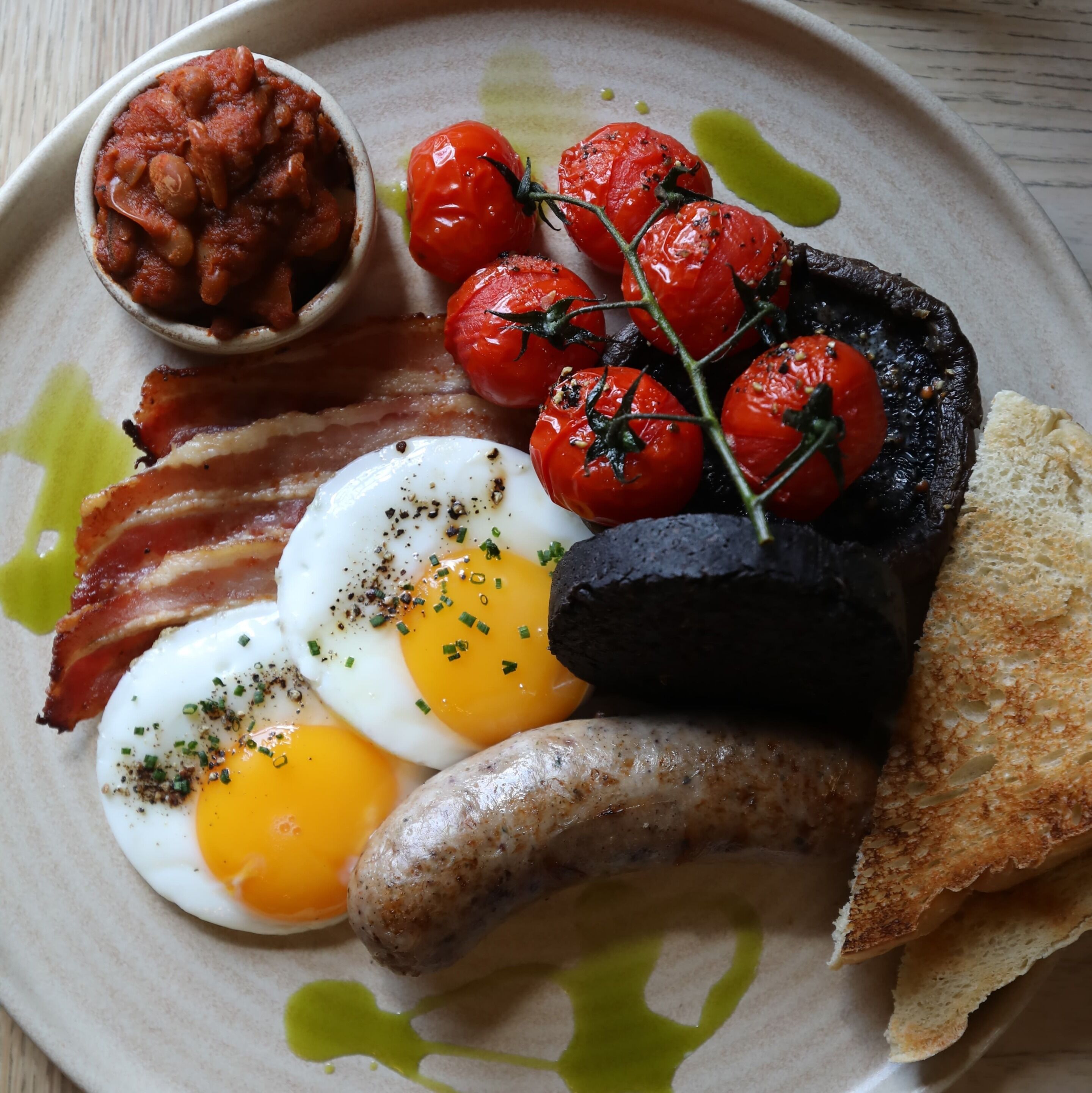 A plate with eggs, sausages, tomatoes, bacon, and toast.