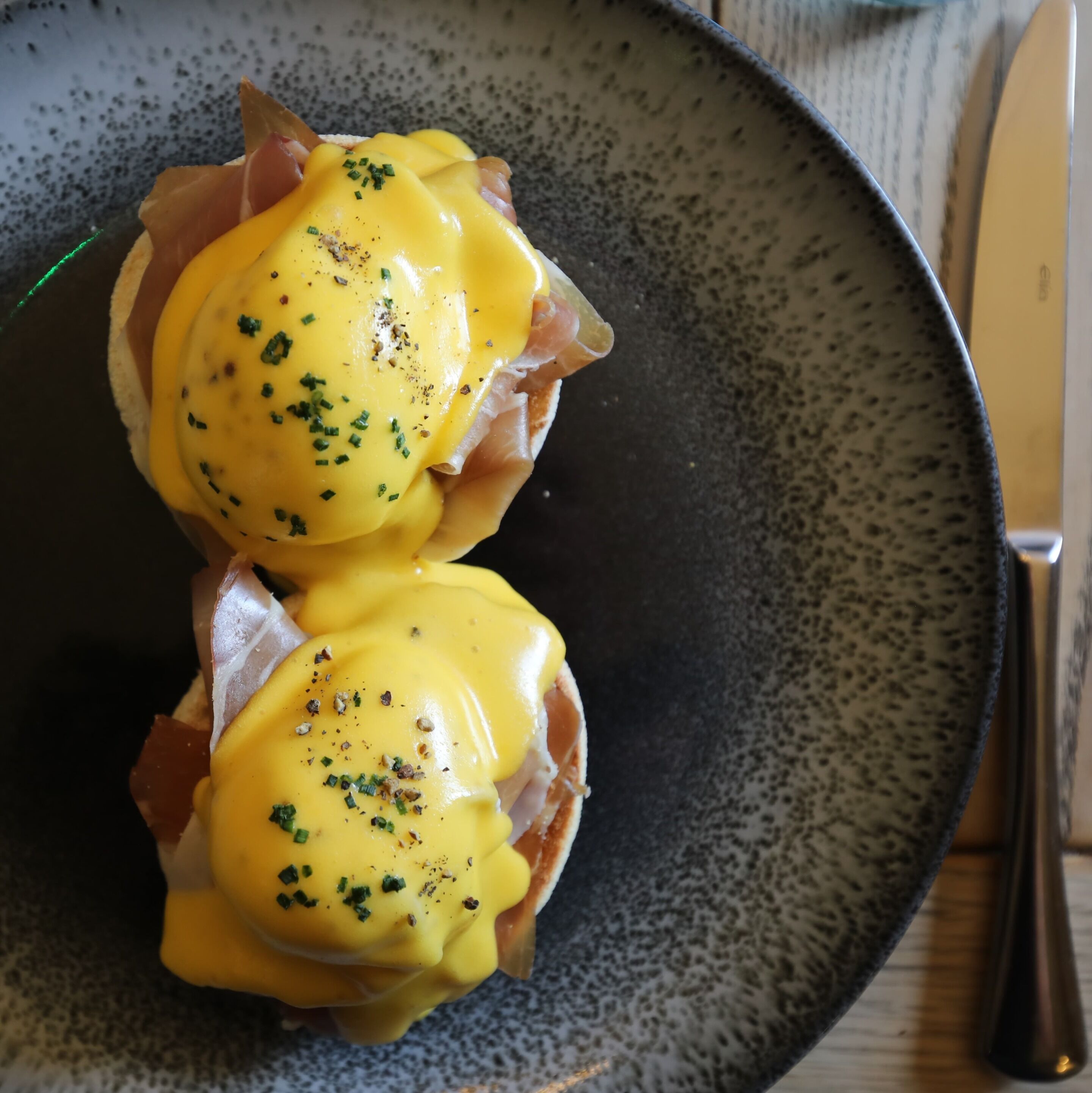 Two eggs benedict sandwiches on a speckled plate.