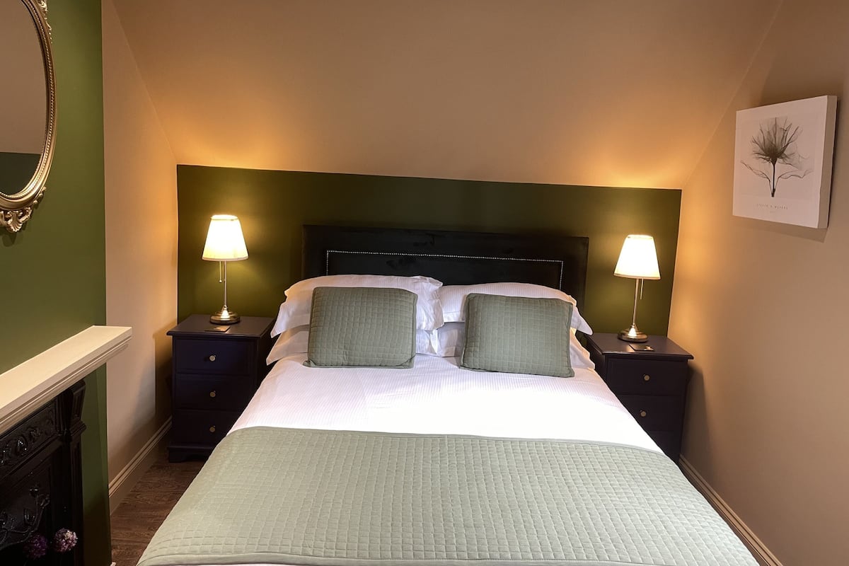 Quarto de hotel bem arrumado com uma cama grande, duas mesas de cabeceira com luminárias, um espelho e uma obra de arte emoldurada na parede.