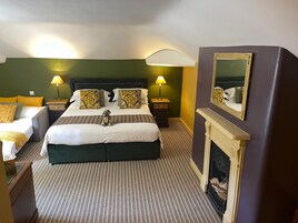 Una habitación de hotel con una cama grande, dos mesitas de noche con lámparas, un espejo y una chimenea.