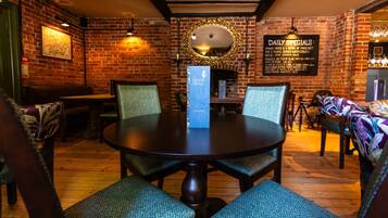 A restaurant with a brick wall, wooden tables, and chairs. There is a menu board on the wall and a mirror above the table.