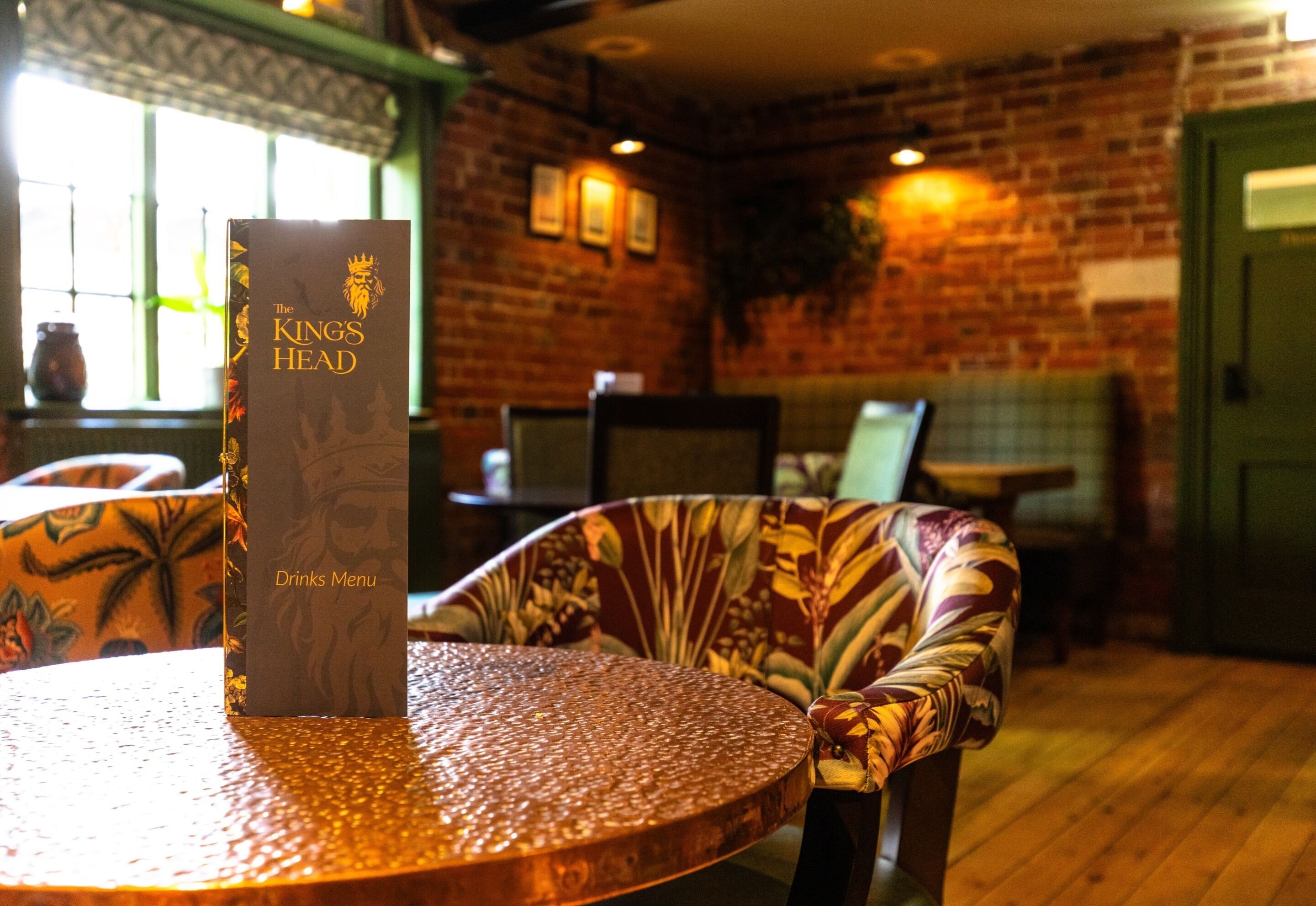 A menu stand with a drinks menu titled "The King's Head" in a restaurant with brick walls and wooden flooring.
